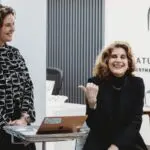 Two women talking inside a medical spa with a logo on the wall.