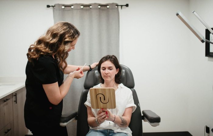 An esthetician consults a client holding a mirror in a medical spa treatment room.